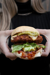 Closeup view of a woman holding a delicious fried chicken burger with guacamole, lettuce, cheese and tomato sauce.