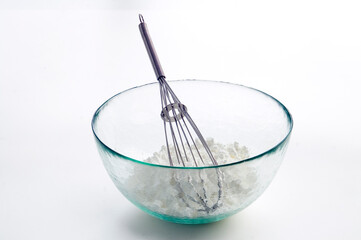 Balloon whisk and flour in glass bowl on white background.