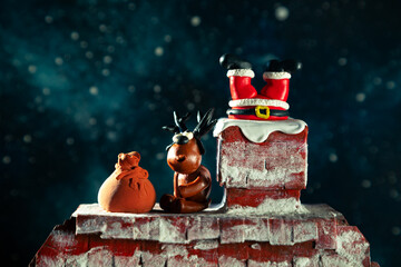 Santa's legs are sticking out of the chimney. Funny plasticine deer sits nearby.