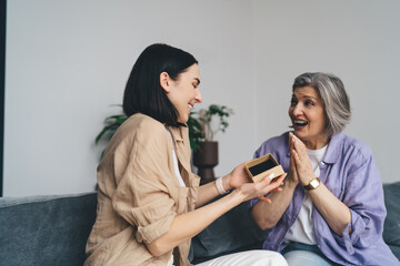 Cheerful mature woman watching female friend opening gift box