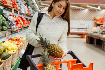 Young woman in the supermarket to buy pineapple, put into cart