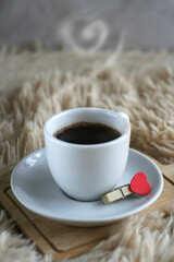 A cup of black strong coffee stands on a wooden board on a soft blanket. Breakfast