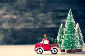 Christmas Car carrying fir tree over wooden background with New Year spruce trees