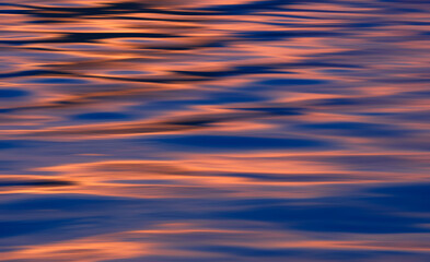 Background abstract colorful motion blur of ripples with dusk sky reflection on sea surface after sundown