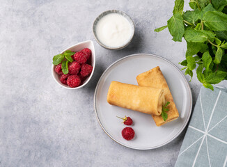 Homemade crepes with raspberry and sour cream on a blue plate on a light background with fresh mint.