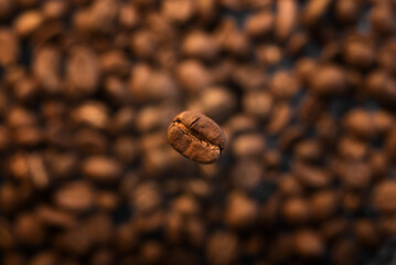 Fototapeta premium Falling hot coffee beans, top view. Roasting coffee beans close-up on coffee background.