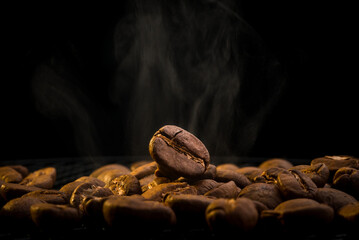 Macro photography with hot grain. Coffee beans on a black background. Roasted coffee beans with smoke. The process of roasting coffee beans close-up.