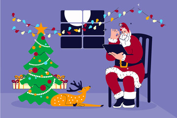 Fototapeta premium Santa Claus sitting on chair with laptop in living room