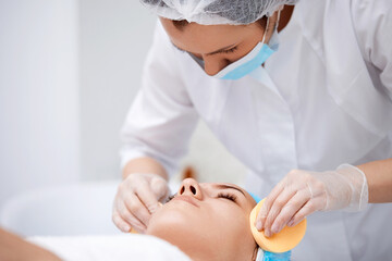 beautician cleanses skin of beautiful woman with a sponge.