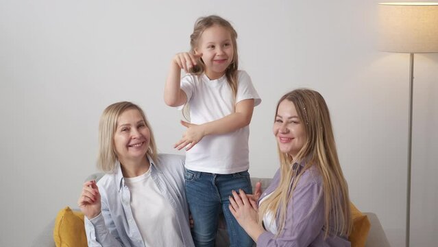 Photo shooting. Happy family. Female generation. Cute smiling girl dancing having fun with mother and grandmother in light room interior slow motion.