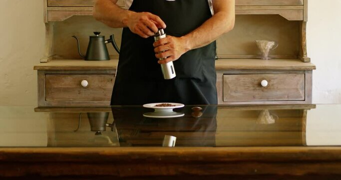 Man in black apron grinding coffee by a manual grinder in slow motion.