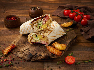 Shawarma chicken roll in a pita with fresh vegetables and cream sauce on wooden background.