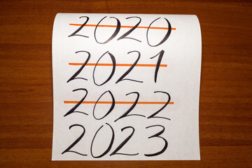 A sheet of paper with the years 2020, 2021, 2022 crossed out and 2023 not crossed out, on a wooden background. The new year is coming.