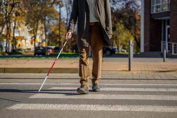 Blind man close-up with a walking stick crosses the road across the pedestrian crossing