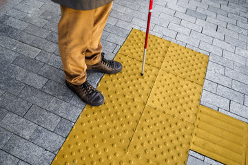 Close-up of a blind man with a walking stick. Stands on a tactile tile for self-orientation while...