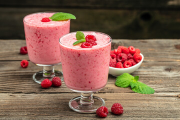 Yogurt smoothie with raspberries in glass on wooden table.