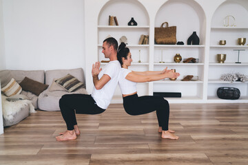 Cheerful young woman and trainer practicing yoga in spacious room
