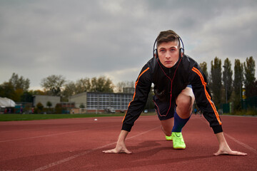 Full length of male athlete listening music while taking position at running track