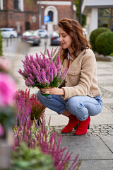Young beautiful woman holding a pot with blooming violet heather plant in a street flower shop.