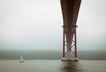Low angle of underneath the Golden Gate bridge in San Francisco, California with a sailboat nearby - obrazy, fototapety, plakaty