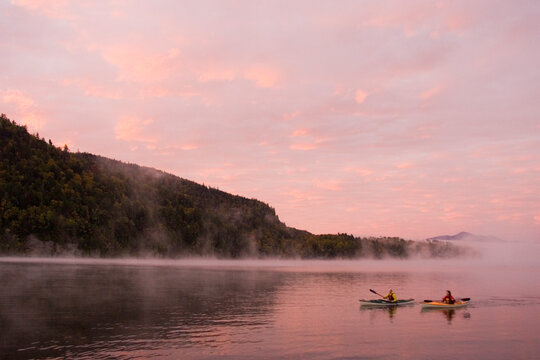 Fit, middle-age couple sea-kayak on Lake Placid at sunrise in autumn, New York, USA