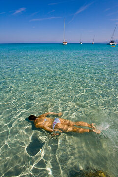 A young woman swims underwater in a crystal clear sea in front of the Saleccia Beach, Corse, France.