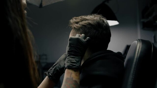 Tattoo piercing studio - a woman makes an ear piercing to a man to a guy