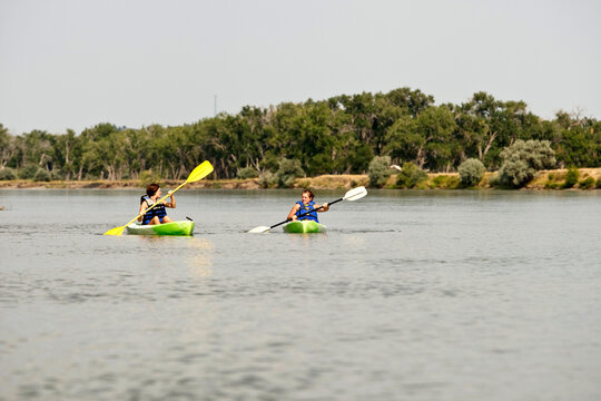 Two girls in life jackets paddle their green kayaks along the Yellowstone River in Eastern Montana.
