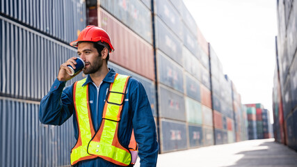 Engineer or foreman standing on the container yard warehouse and drinking coffee on rest time.