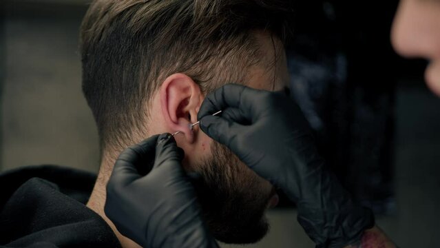 Tattoo piercing studio - a woman makes an ear piercing to a man to a guy