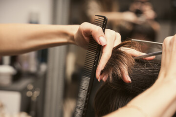 Hairstylist does cutting hair tips of a female customer in a beauty salon. Womens fashion and...