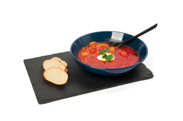 red borscht in a dark blue plate with a spoon inside, standing on a black slate board on a white background