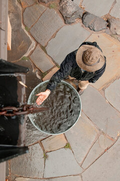 View from above of a woman standing by a rain catchment barrel, holding her hand out.