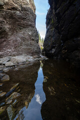a dark rocky valley in Norway, Helvete, where between rocky gray rocks there is water reflecting the blue sky and some green bushes