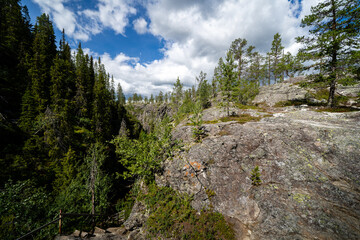a rocky slope in the norwegian mountains covered with majestic green forests above which is a beautiful blue sky with fabulous clouds