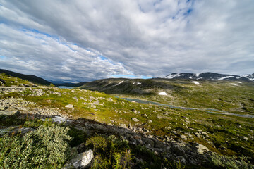 Norway Stryn mountain peak, green moss covered stone and snow visible on the mountain tops in sunny summer when there is a blue sky above the mountains with lots of fluffy clouds