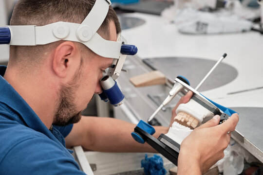 Dental technician working with articulator in dental laboratory.