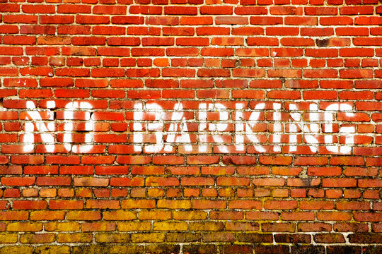 Fototapeta NO BARKING sign painted on the wall of a bright red brick building.