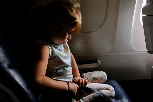little girl putting on airplane seatbelt in dramatic light