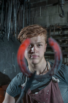 Apprentice blacksmith with hammered red hot horseshoe at workshop