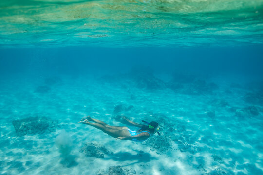Female swims underwater in blue Hawaiian waters