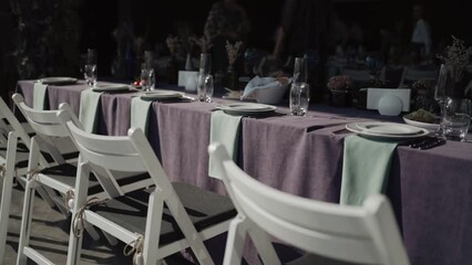 Romantic dinner with Banquet table and white chairs. Outdoors Party on the nature. Celebration event. Beautiful decoration on tables. Gourmet and luxury dinner. Festive table setting.