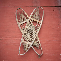 Hand made old snowshoes hung on an old red wooden building