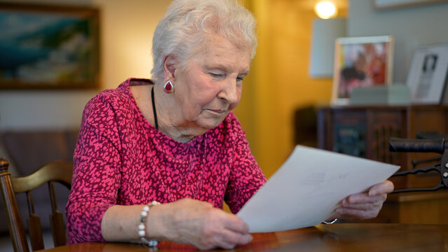 Elderly senior woman smiling and sitting at table looking at photo memories.