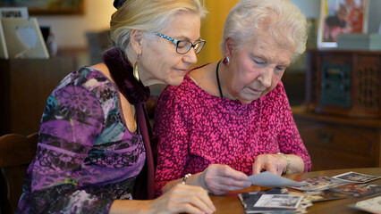 Closeup of senior elderly smiling woman looking at old photos and remembering memories with daughter at the dining room table.