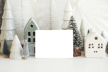 Christmas card and little scandinavian village. Empty greeting card and christmas trees and houses decorations on white table. Postcard template with space for text. Happy Holidays!