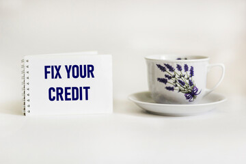 Fix Your Credit text written on notepad and white background with beautiful tea cup .Conceptual photo. Evaluation tips fix improvement