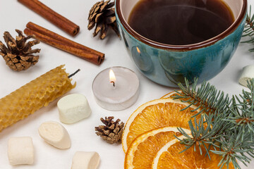 Obraz na płótnie Canvas A mug of coffee, a lit candle, a spruce branch, cones and dry orange slices.