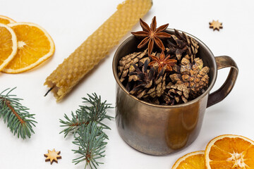 Cones in a metal mug, a candle, sprigs of spruce and dry orange slices.