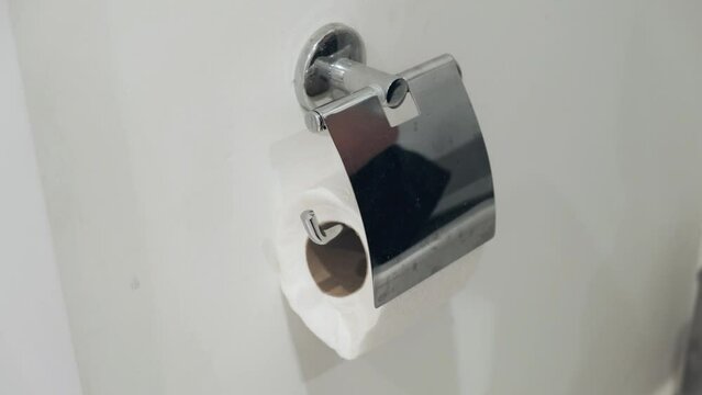 Hands taking toilet paper from a wall mounted toilet paper roll dispenser. Stainless steel Bumf holder in bathroom. lavatory interior element.